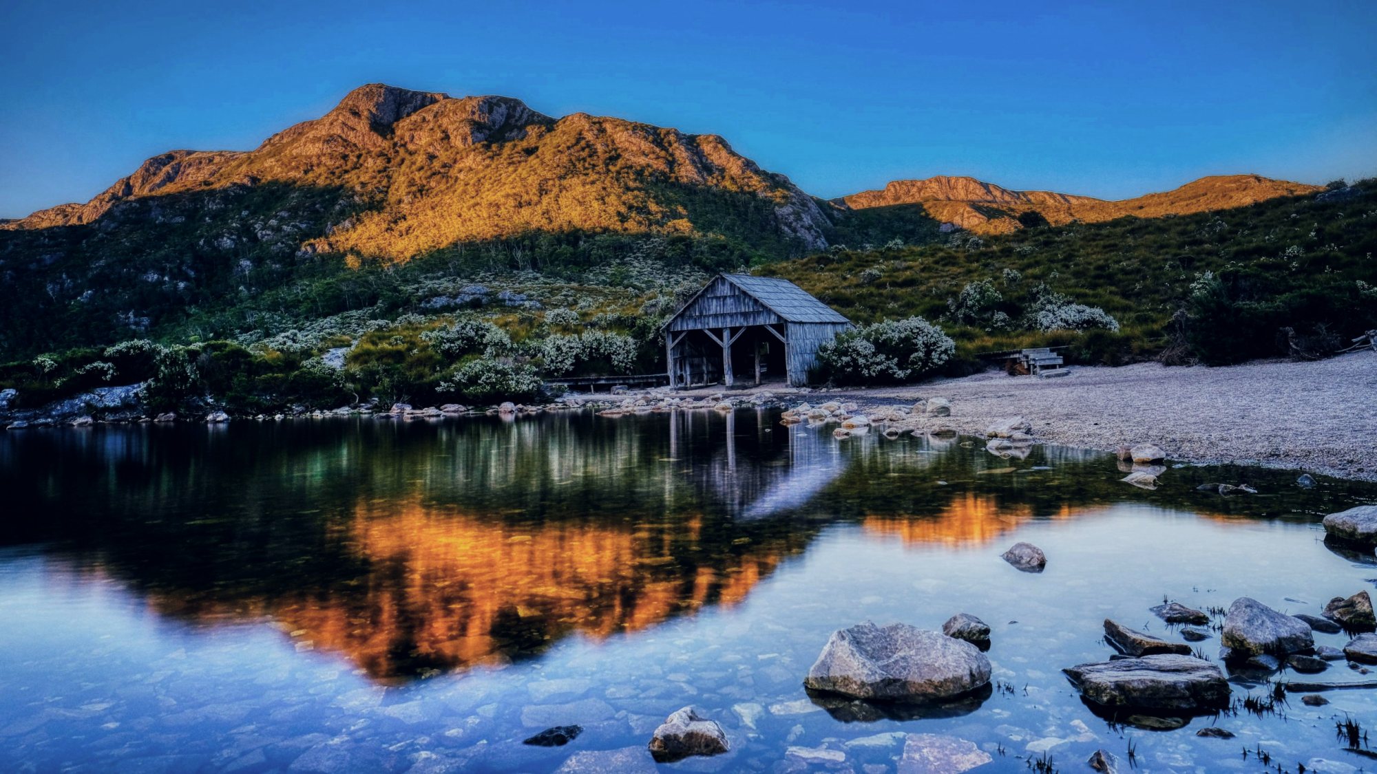 Boatshed reflected in still water below Cradle Mountain